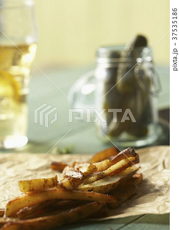 Fries on Parchment Paper; Jar of Pickles; Glass of Beer 37535186