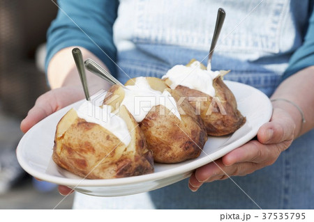 A person holding a plate of jacket potatoes with sour cream A person holding a plate of jacket potatoes with sour cream 37535795