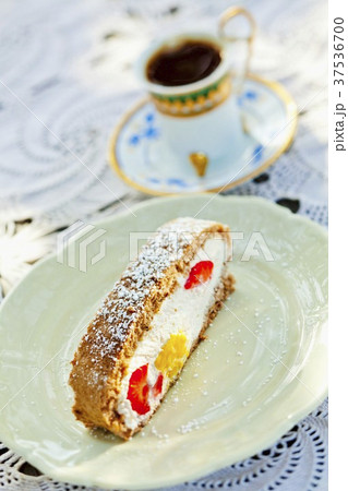 A slice of wholemeal sponge cake, filled with quark cream, mango and strawberries with a cup of mocha in the background 37536700