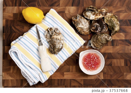 Raw Oysters with Hand Towel, Shucking Knife and Lemon; On Cutting Board 37537668
