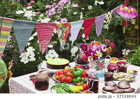 A table laid in a garden with biscuits, fresh vegetables, jam and cake 37538043