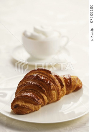 A croissant on a plate with a cappuccino in the background A croissant on a plate with a cappuccino in the background 37539100