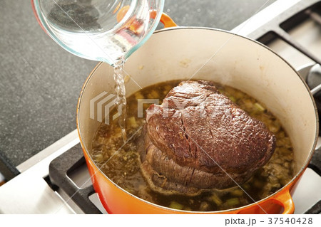 Pouring Water into a Pot of Broth with a Pot Roast 37540428