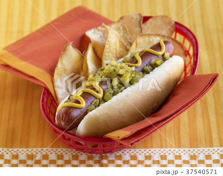 Hot Dog Topped with Relish and Mustard with Chips in a Plastic Take-Out Basket Hot Dog Topped with Relish and Mustard with Chips in a Plastic Take-Out Basket 37540571