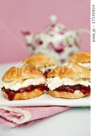 Scones with strawberry jam and cream with a pot of tea in the background Scones with strawberry jam and cream with a pot of tea in the background 37540834