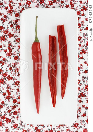 A whole and a halved chilli pepper on a plate (seen from above) 37542542