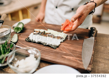 Male cook making sushi on wooden table, asian food Male cook making sushi on wooden table, asian food 37554392