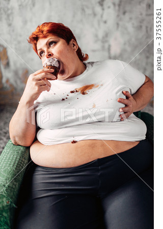 Overweight woman sits in chair and eats sweet cake 37555261