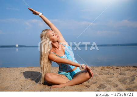Blonde girl in a blue suit is doing yoga on beach Blonde girl in a blue suit is doing yoga on beach 37556721