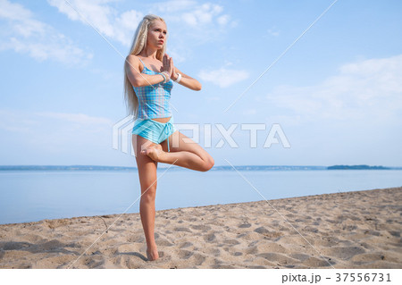 Blonde girl in a blue suit is doing yoga on beach 37556731