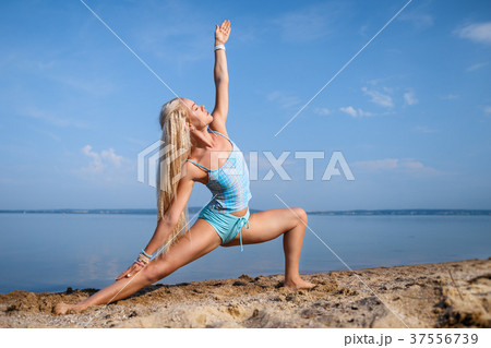 Blonde girl in a blue suit is doing yoga on beach Blonde girl in a blue suit is doing yoga on beach 37556739