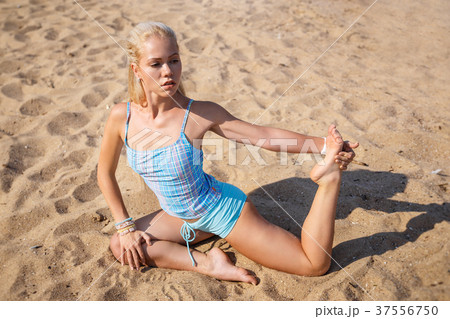 Blonde girl in a blue suit is doing yoga on beach Blonde girl in a blue suit is doing yoga on beach 37556750