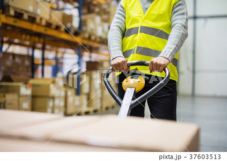 Male warehouse worker pulling a pallet truck. 37603513