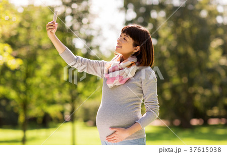 happy pregnant asian woman taking selfie at park happy pregnant asian woman taking selfie at park 37615038