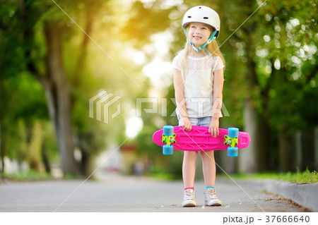 Pretty little girl learning to skateboard on beautiful summer day in a park Pretty little girl learning to skateboard on beautiful summer day in a park 37666640