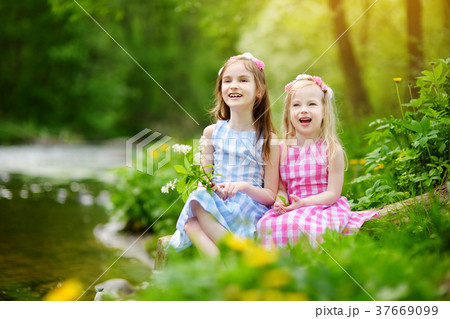 Two adorable little sisters playing by a river in sunny park on a beautiful summer day Two adorable little sisters playing by a river in sunny park on a beautiful summer day 37669099