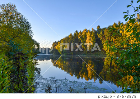 autumn forest is reflected in the calm blue water autumn forest is reflected in the calm blue water 37673878