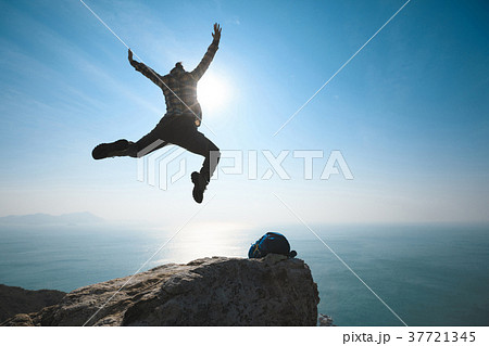 free hiker jumping on sunrise seaside cliff edge 37721345