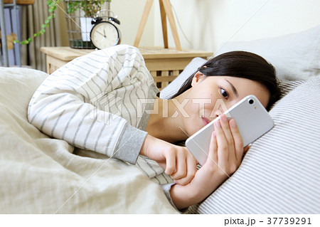 寝室でスマートフォンを見る女性 37739291
