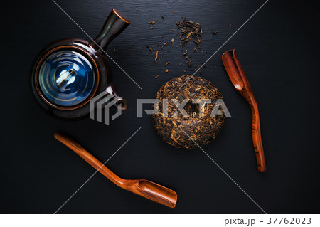 Tea pot and green dry tea on black table 37762023