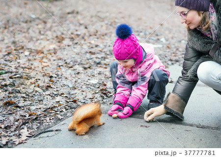 Girl with mom feeding squirrel in a forest. 37777781