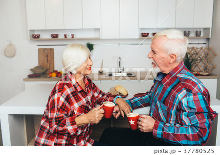 Elderly man and woman drink latte at the kitchen Elderly man and woman drink latte at the kitchen 37780525