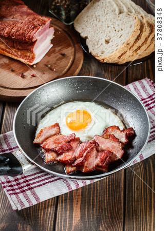 Slices of smoked bacon and fried egg in frying pan 37808348