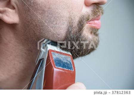 Close up young man shaving with electric razor 37812363