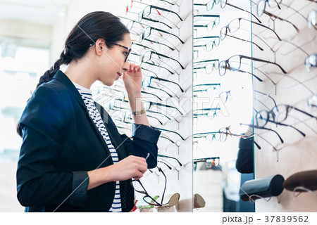 Woman taking glasses off shelf in optician shop 37839562