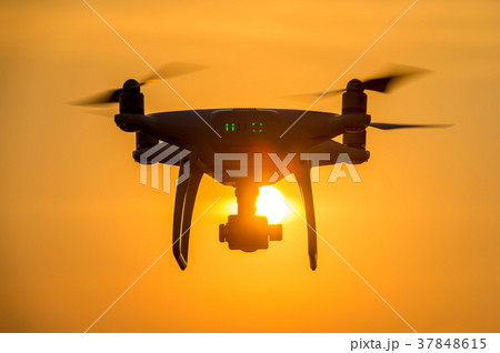 Silhouette drone with camera flying at sunset. Silhouette drone with camera flying at sunset. 37848615