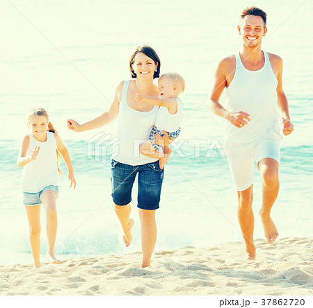 family of four running on sandy beach on sunny weather 37862720