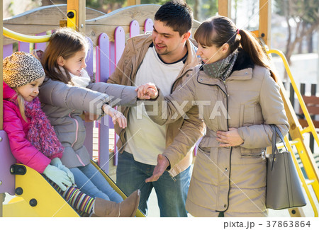 parents playing with little daughters at slide of playground parents playing with little daughters at slide of playground 37863864