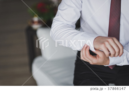Young man buttons cuff link on the sleeve of his shirt 7947. 37866147