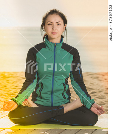 woman doing yoga poses cross-legged on beach in morning 37867152