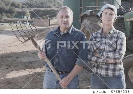 Serious mature spouses farmers posing near tractor 37867553