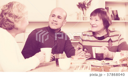 Smiling aged friends are sitting at table with tea and talking about life Smiling aged friends are sitting at table with tea and talking about life 37868040