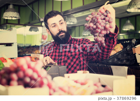 Glad male seller offering grapes in shop 37869296
