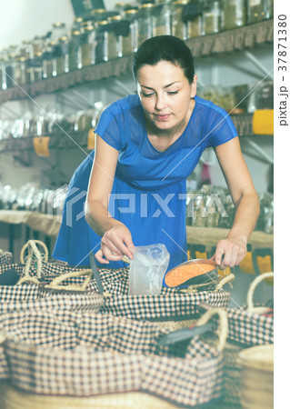 female customer taking сereals with scoop from basket in eco market 37871380