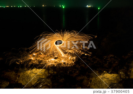 Man showing spinning fire on rocky beach at night 37900405