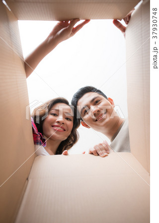 Smiling young couple opening a carton box Smiling young couple opening a carton box 37930748
