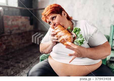 Fat woman sits in chair and eats sandwich, bulimic 37943408