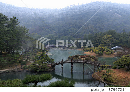 栗林公園 冬の南庭南湖 雪の紫雲山 手前は偃月橋 中央奥は掬月亭 の写真素材