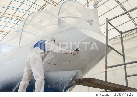 Man wearing protective uniform and spraying paint to the boat, Maintenance concept 37977826