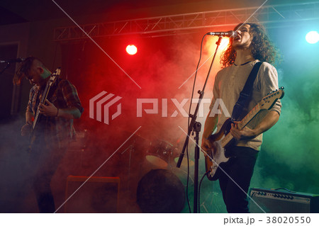 Rock band performs on stage. Guitarist, bass guitar and drums. 38020550