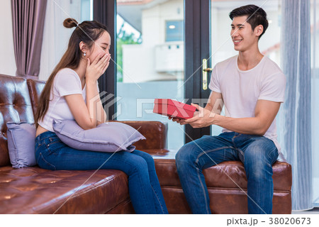 Boyfriend surprising girlfriend with present. Woman surprised wh Boyfriend surprising girlfriend with present. Woman surprised wh 38020673