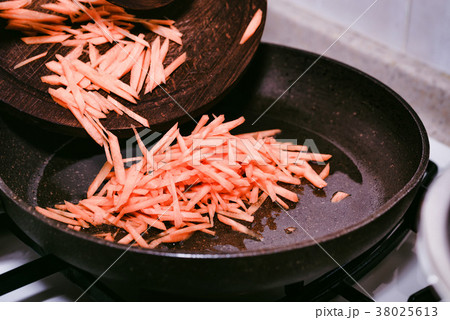 Female hands add chopped carrot to frying pan 38025613