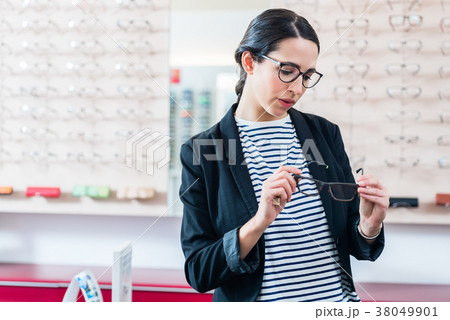 Woman taking glasses off shelf in optician shop 38049901