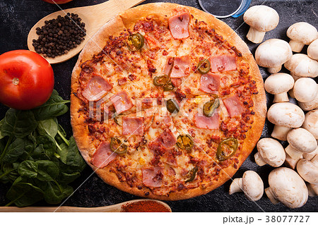 Top view on hot pizza next to ingredients which it Top view on hot pizza next to ingredients which it 38077727