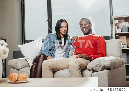 Glad couple sitting and hugging on sofa inside 38125092
