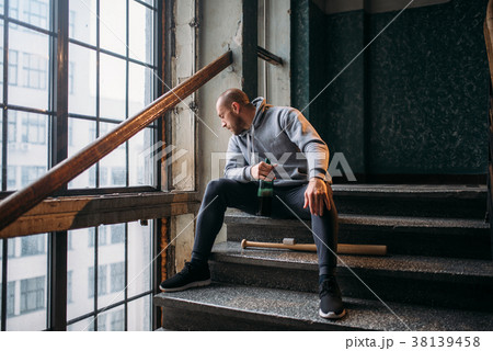 Male theif with baseball bat sits on stairs Male theif with baseball bat sits on stairs 38139458